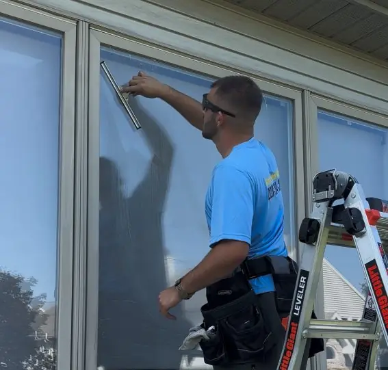 Wizards Window Washing technician cleaning a window from a ladder